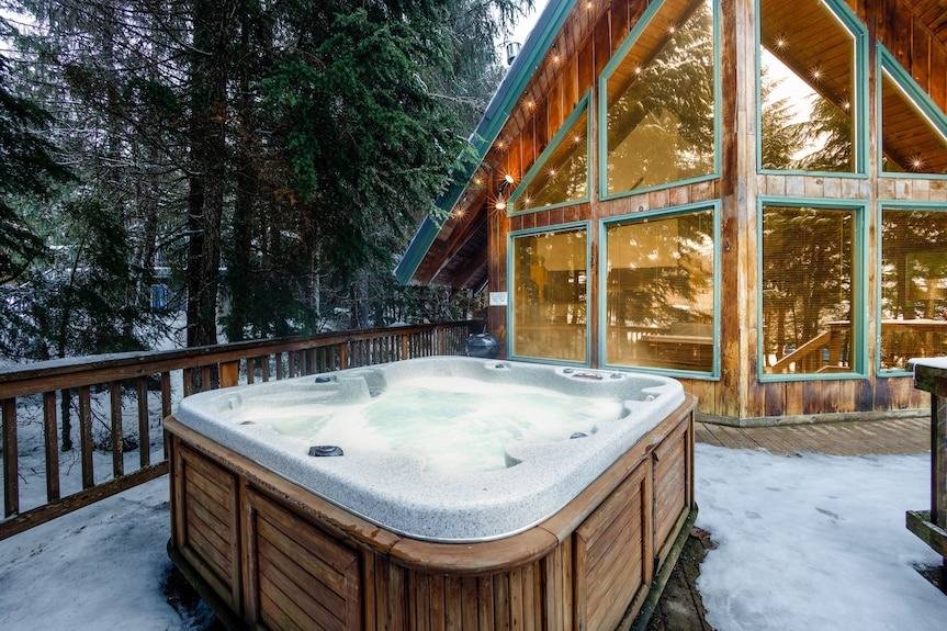 Outdoor hot tub on wooden deck beside forest cabin in winter
